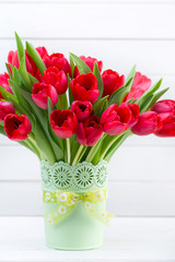 Fresh red tulip flowers bouquet on shelf in front of wooden wall.