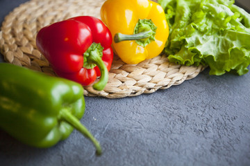 Heathy food Vegetarian Concept. Lettuce leaves on a table mat and red, green and yellow paprika peppers on a dark concrete background with copy space