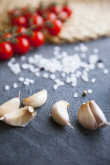 Diet, Italian Food Cooking, Vegetarian Concept. Fresh cherry tomatoes, garlic cloves and sea salt grains, rattan table mat and dark concrete as a background, selective focus