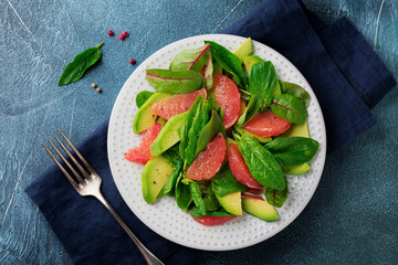 Useful tasty salad of spinach, chard, avocado and grapefruit with olive oil on an old concrete dark background. Selective focus. Top view. Copy space.