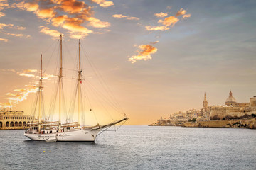 Sunset with a yacht in Valletta, capital city of Malta, known in Maltese as Il-Belt. Scenic city view from the bay with a ship in front. - obrazy, fototapety, plakaty