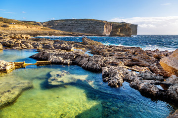 Malta, Gozo Island. Beautiful limestone cliffs facing the ocean near Dwejra Bay with water pools and riffs as seen from the Azure Window. - obrazy, fototapety, plakaty