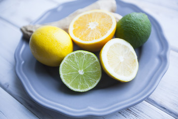 Healthy Food, Tea, Cold Treatment Concept. Green limes,lemons and a ginger root on a blue plate, white wooden background, close up