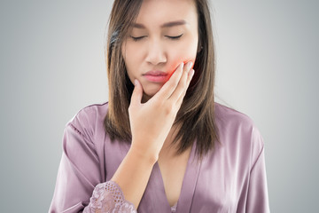 Suffering from toothache. Beautiful young woman suffering from toothache while standing against grey background