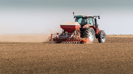Farmer with tractor seeding - sowing crops at agricultural fields