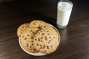 Chocolate chip cookies and glass of milk on wooden table