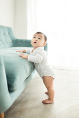 Fototapeta premium Sweet baby girl standing by the sofa at home.