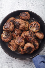 Vertical closeup of traditional swedish beef meatballs served in one portion black cast iron pan, handle wrapped in blue towel. Textured background.