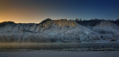 Winter frosty morning before dawn. Freezing river from the hilly banks and large ice floes.