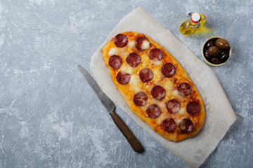 Oval Italian pizza with tomato and salami Pepperoni on gray concrete background. Selective focus....