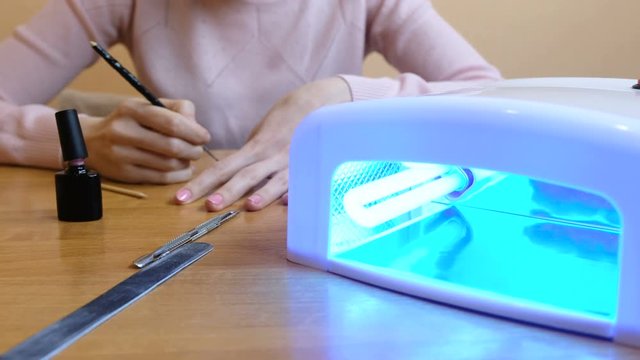 Young woman doing yourself a manicure in the background. In the foreground is the uv lamp. 4K