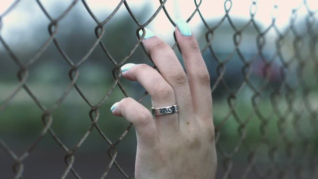 Female hand with ring and blue manicure touching fence mesh walk on street. Close up woman hand touching fence mesh on street. Woman freedom concept