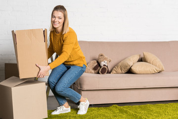 woman holding cardboard box and smiling at camera while relocating