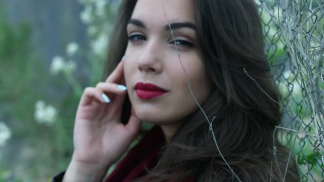 Portrait beautiful woman with brunette hair looking in camera on fence mesh. Close up attractive woman with sexy lipstick. Face young woman with sexy make up