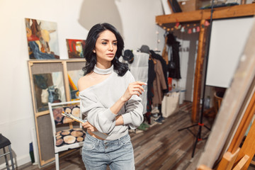 Smiling girl paints on canvas with oil colors in workshop