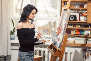 Smiling girl paints on canvas with oil colors in workshop