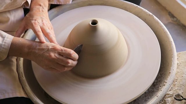 High angle view of female potter carving clay with blade on pottery wheel