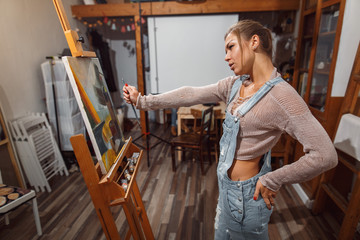 Smiling girl paints on canvas with oil colors in workshop