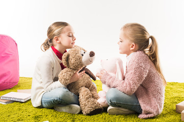 little sisters playing with soft toys while sitting on floor isolated on white