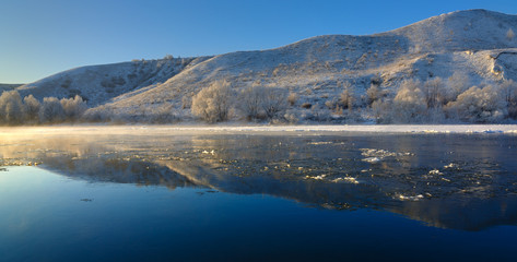 Fototapeta na wymiar Freezing river from the hilly banks and large ice floes. A sunny day with a cloudless sky.