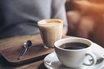 Closeup image of a cup of Americano coffee and a glass of latte coffee on vintage wooden table in cafe