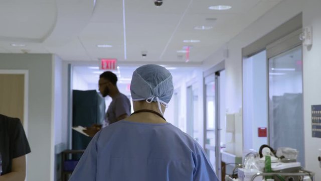 Handheld shot of doctor wearing scrubs walking by colleagues in corridor at hospital