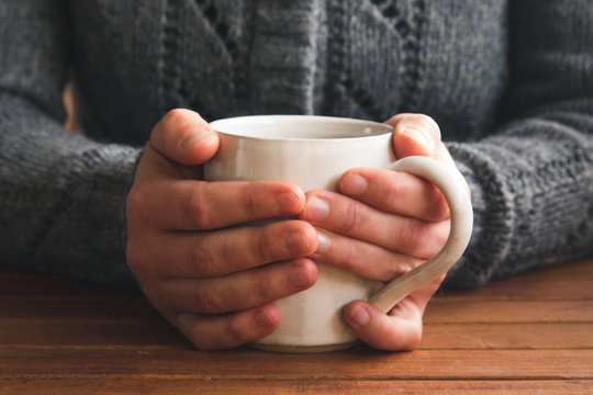 Woman holding mug of tea wearing cozy gray cardigan at a table