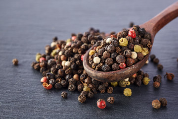 Black food background with spices. A mixture of peppers with a wooden spoon on a shale stone.