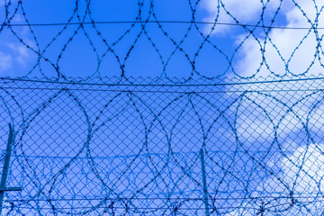 Gray fence with barbed wire in the background of a blue sky with clouds