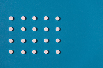 Pattern with white tablets and one colored tablet On Blue Background With Copy-Space. Medicine Healthcare Pharmacy Concept