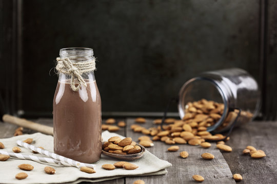 Organic chocolate almond milk in a glass bottle with whole almonds spilled over a rustic wooden table.