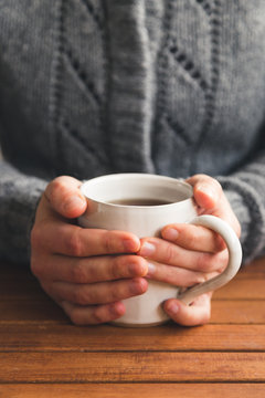 Woman sat at table with mug of tea wearing cozy gray cardigan
