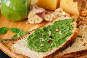 Bruschetta with basil walnut pesto sauce on a wooden plate. Black stone backdrop.