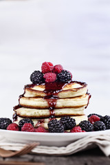 Delicious homemade golden pancakes with fresh blackberries, raspberries, and raspberry syrup. Extreme shallow depth of field.