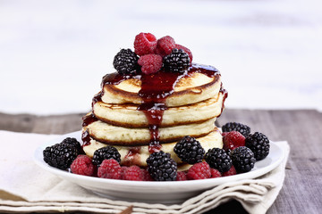 Delicious homemade golden pancakes with fresh blackberries, raspberries, and raspberry syrup. Extreme shallow depth of field.