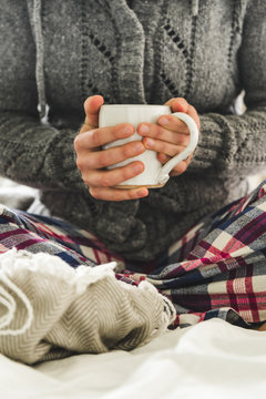 Woman wearing cozy pyjamas sitting on a bed with a mug of tea