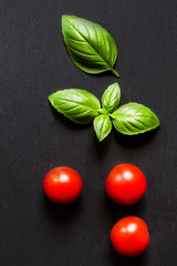 Fresh cherry tomatoes and basil leaf  on black slate stone chalkboard with copyspace. Healthy Italian traditional caprese salad ingredients. Organic Mediterranean food concept, flat lay