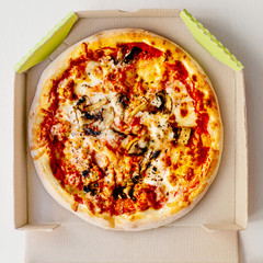 Pizza in a cardboard box on bright  background  with pepperoni, cherry tomatoes, cheese and tomato sauce. Pizza delivery, menu.