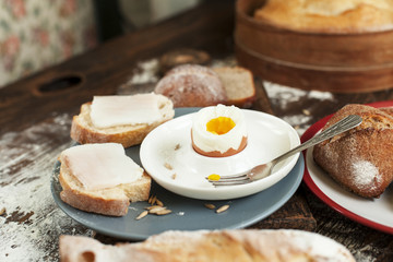 boiled egg on a plate, freshly baked bread and sandwiches with bacon on a wooden table