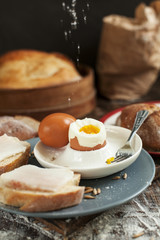 boiled egg on a plate, freshly baked bread and sandwiches with bacon on a wooden table