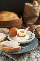 boiled egg on a plate, freshly baked bread and sandwiches with bacon on a wooden table