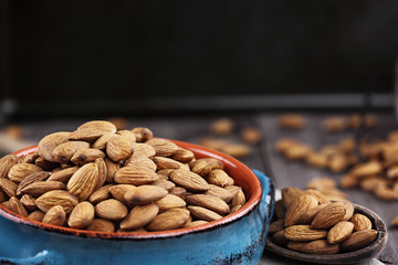 Whole almonds in bowl and wooden spoon against a rustic background.