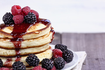 Delicious homemade golden pancakes with fresh blackberries, raspberries, and raspberry syrup. Extreme shallow depth of field.
