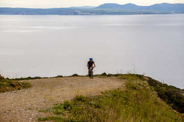 Theme tourism and cycling on mountain biking. guy rides uphill on a rocky, rocky road against the background of the Mediterranean Sea in Spain on the shore of the kosta brava in helmet and sportswear