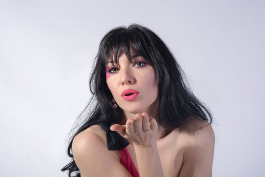 A young playful woman with a heart on her cheek sends an air kiss before the white background