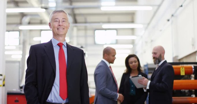 4K Portrait smiling businessman in factory with colleagues standing in background. Slow motion.