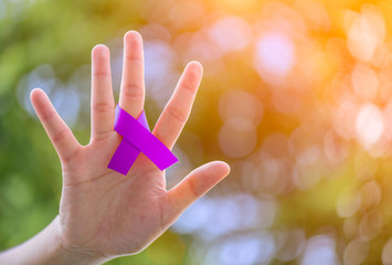  Cancer Awareness campaign. Female hands holding Purple CANCER awareness ribbon on green bokeh...