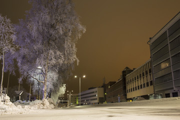 View of a street in Helsinki with tall buildings on the right facing the street and the park with trees to the left. Everything is covered by snow.