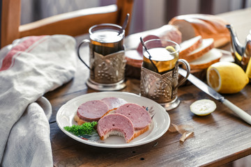 Sandwiches with sliced sausage on a plate with tea