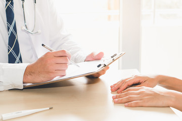 Close up hands of doctor taking note patient history to clipboard and giving diagnosis her disease.